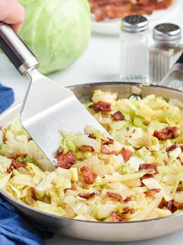 A spatula stirs the cabbage and bacon.