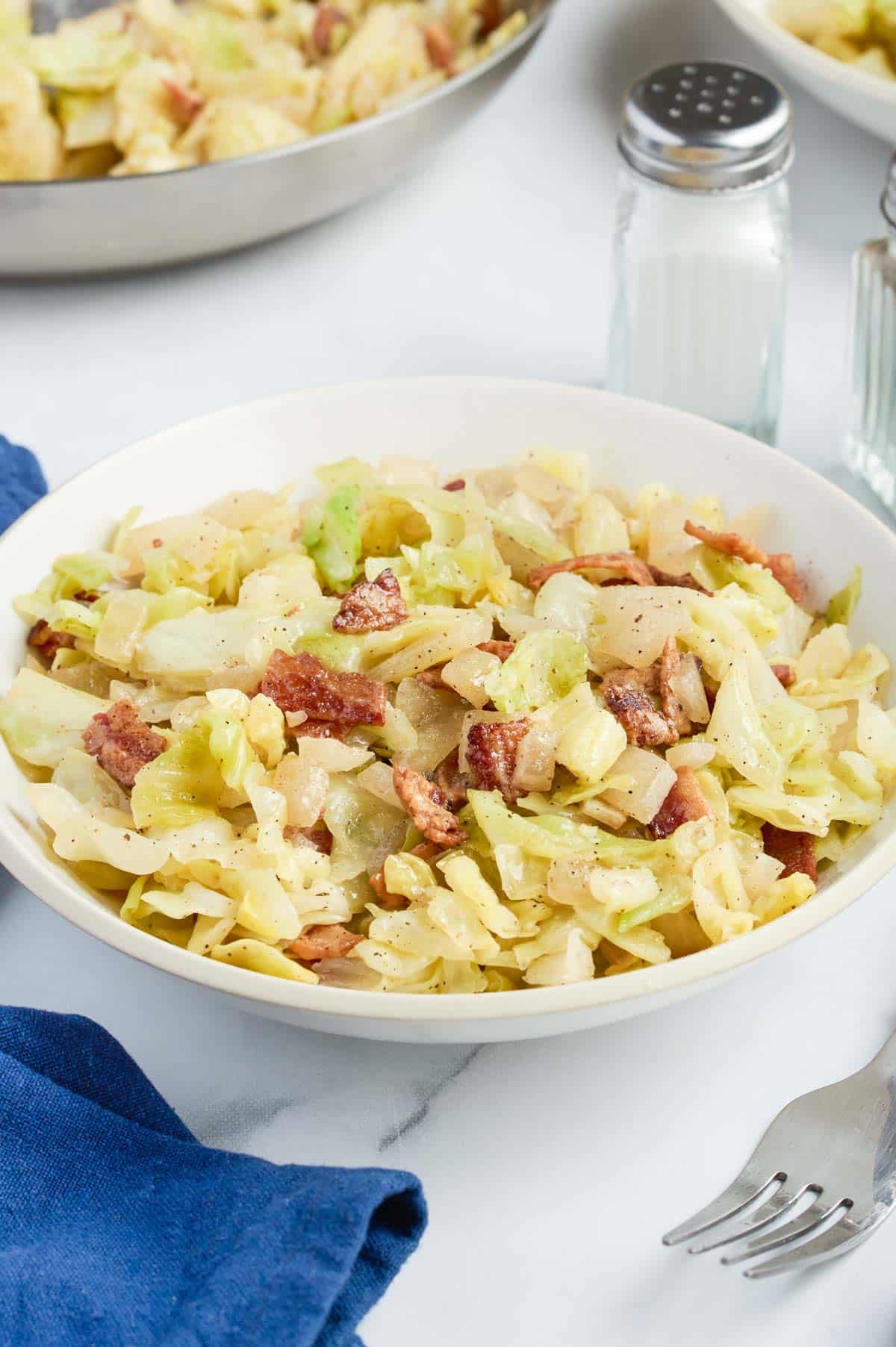 A white bowl is full of fried cabbage with bacon.