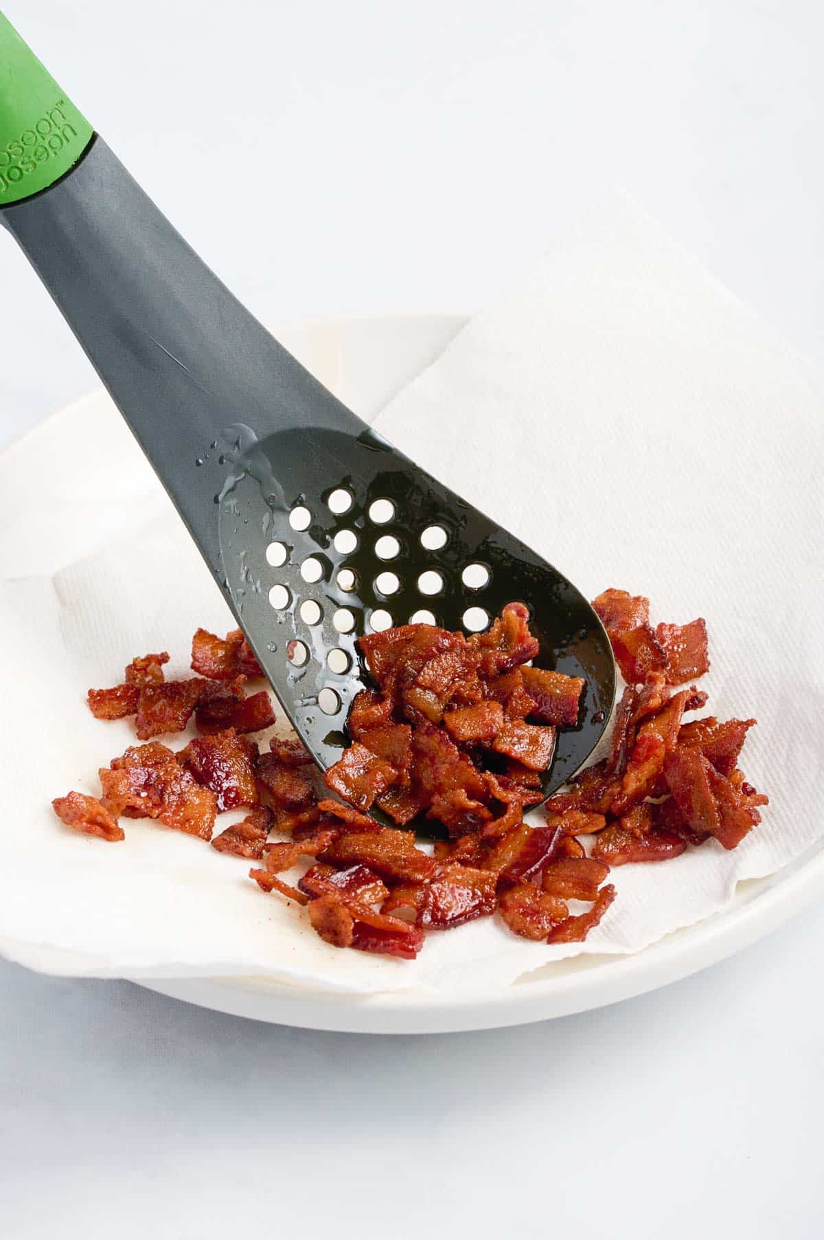Bacon is scooped onto a plate to drain.