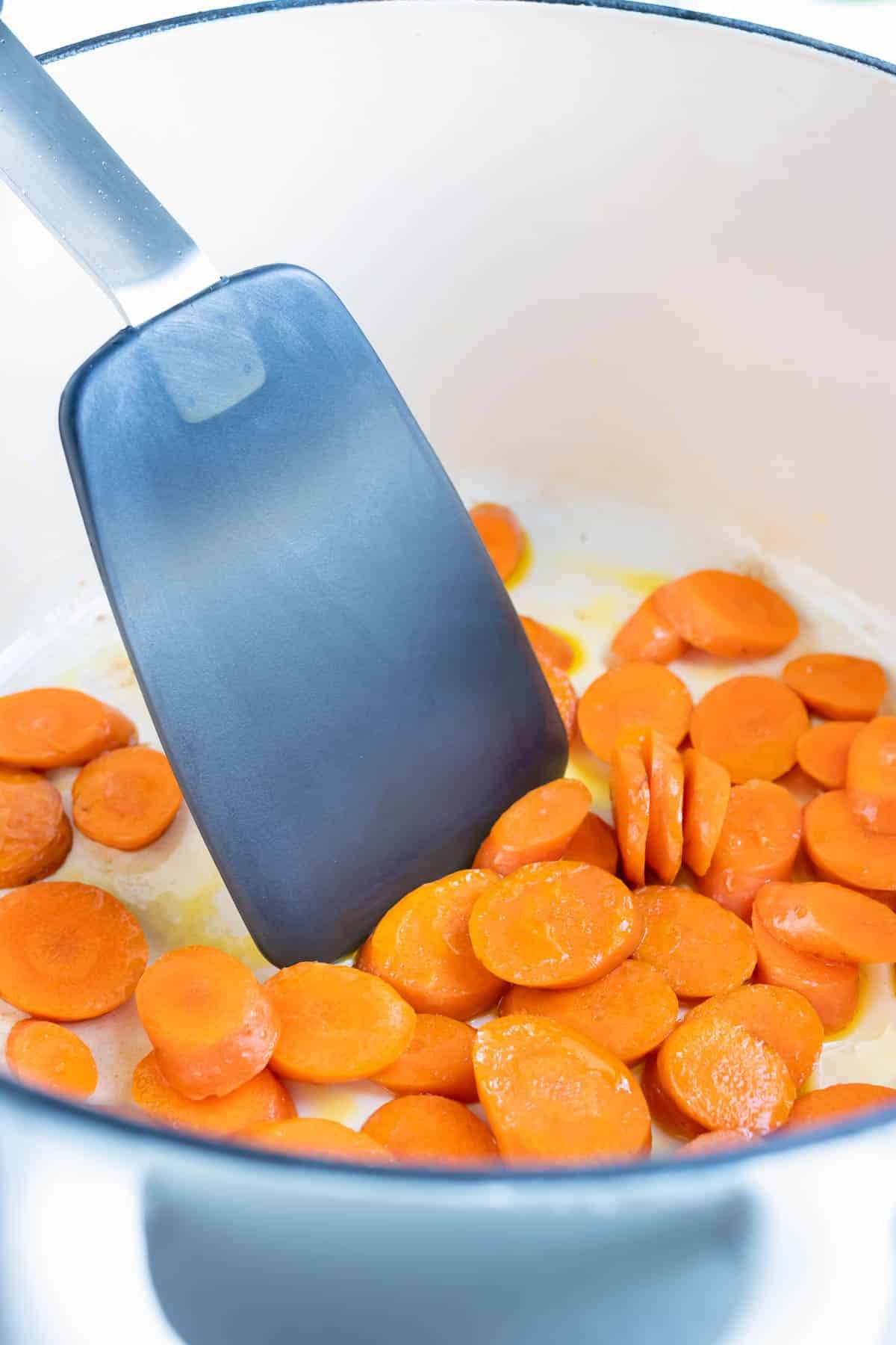 Carrots are sautéed in a pan on the stove.