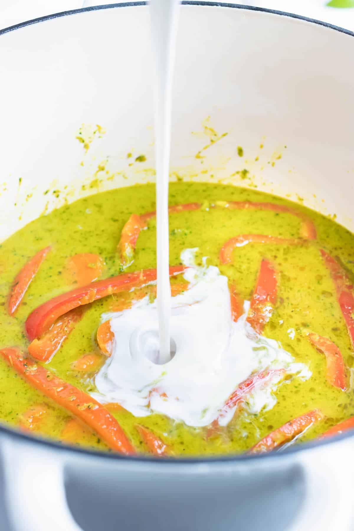 Coconut milk, curry paste, chicken broth, and bell peppers are added to the dutch oven or pot.