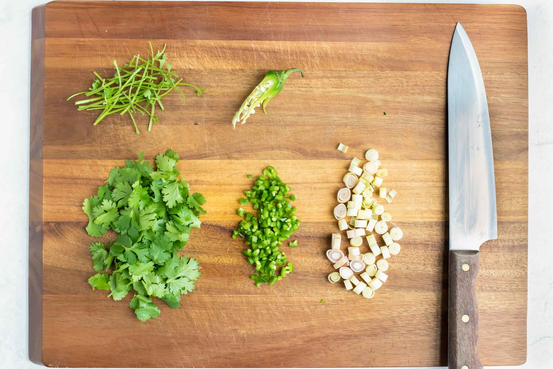 Garlic, cilantro, and peppers are chopped and prepared on a cutting board.