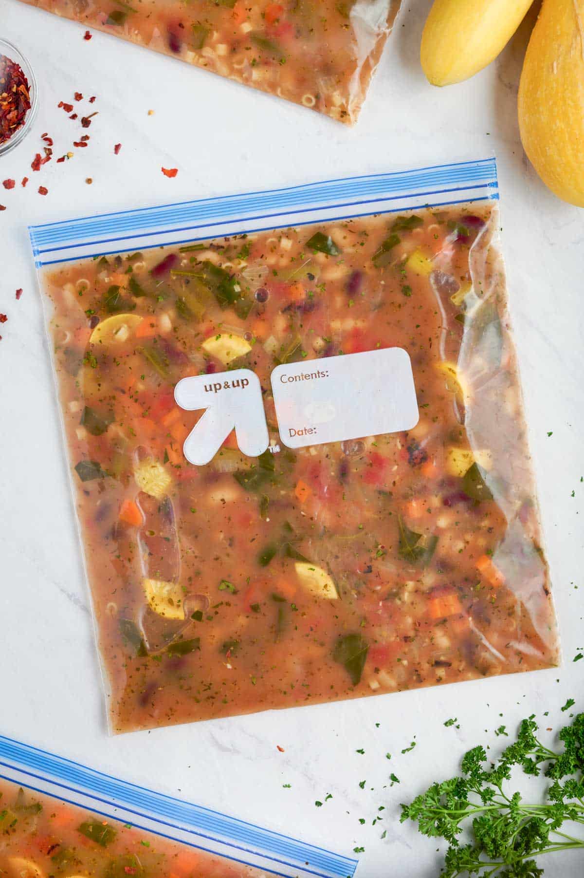 Minestrone soup in a freezer-safe gallon-sized bag laying flat on the countertop ready to be put in the freezer. 