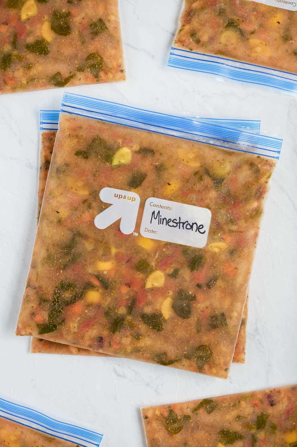 Multiple minestrone soups in a freezer-safe gallon-sized bags laying flat on the countertop frozen.