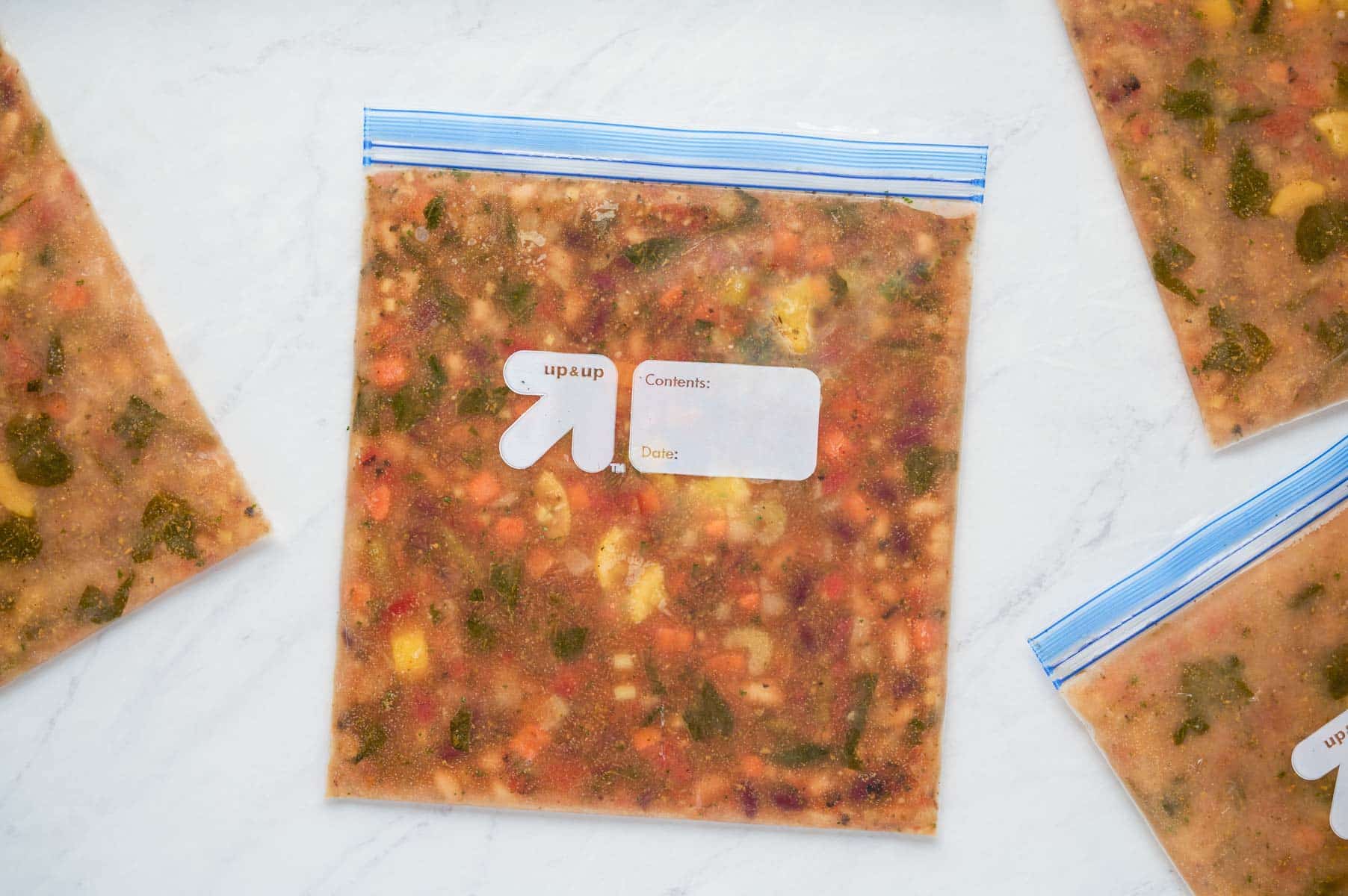 Minestrone soup in a freezer-safe gallon-sized bag laying flat on the countertop frozen.