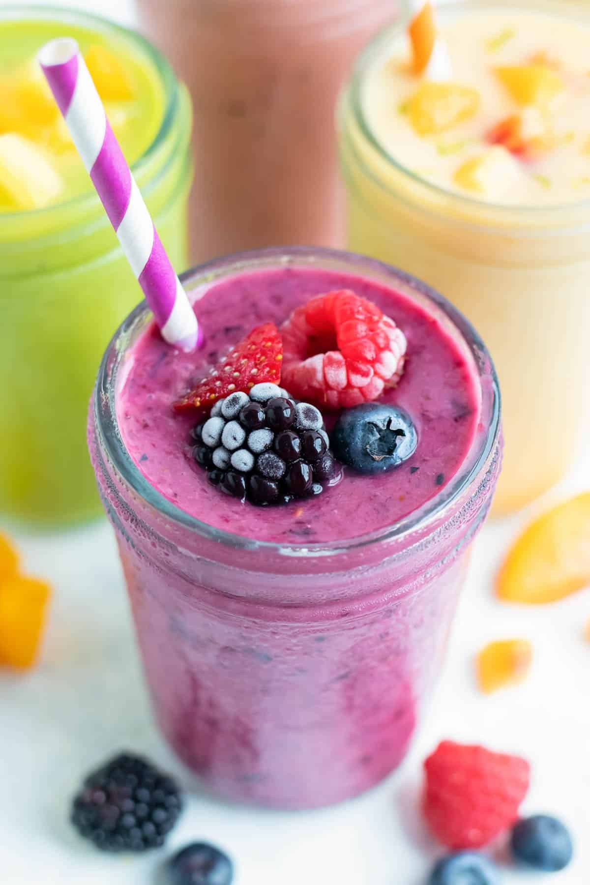 A berry smoothie is on the counter with other smoothies.