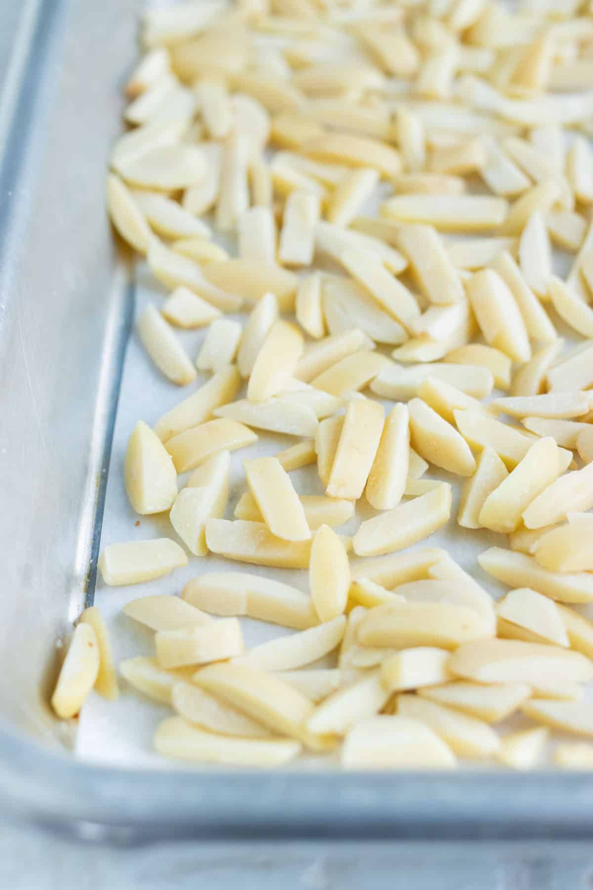 Slivered almonds are spread out on a sheet pan evenly before roasting.