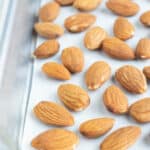Whole almonds are laid out on a baking sheet in a single layer to be roasted in the oven.