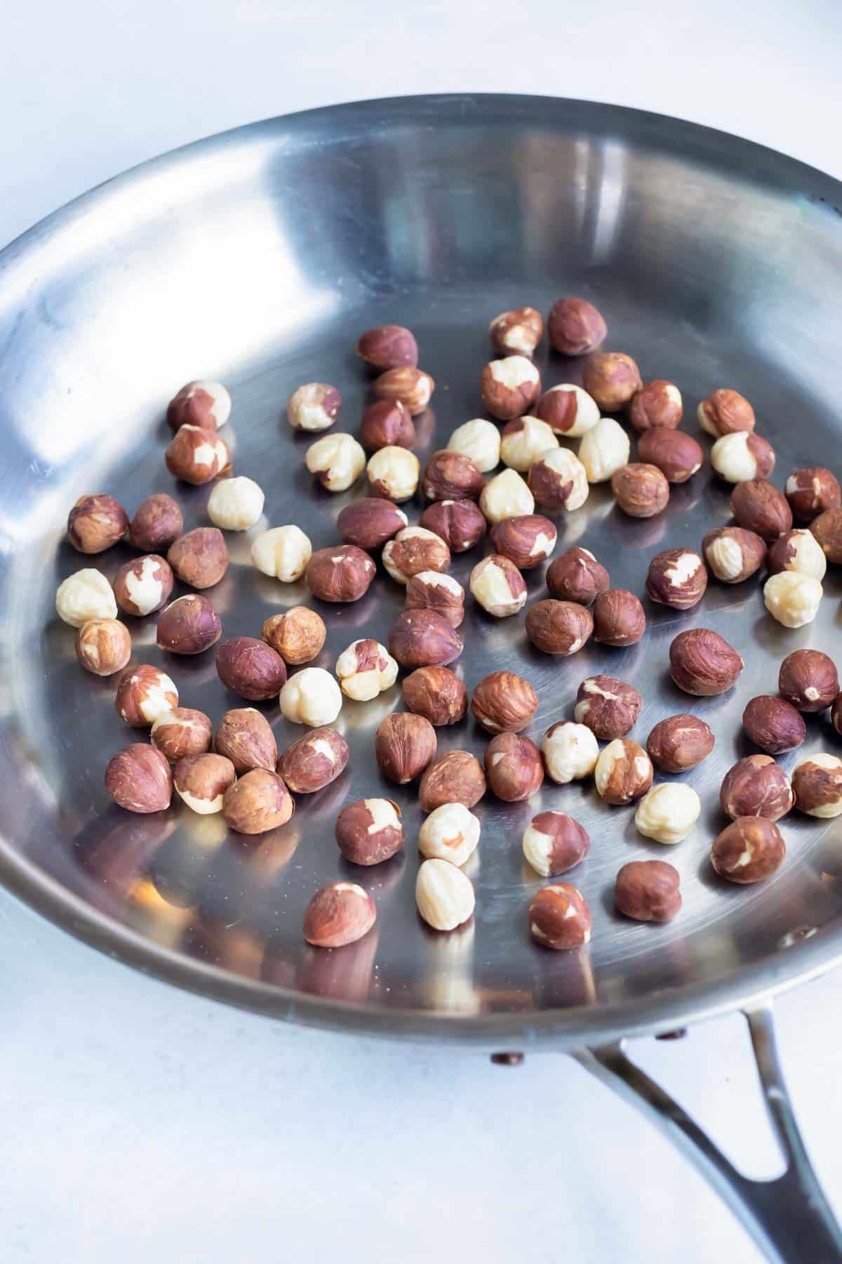 Hazelnuts are roasted in a skillet on the stovetop.