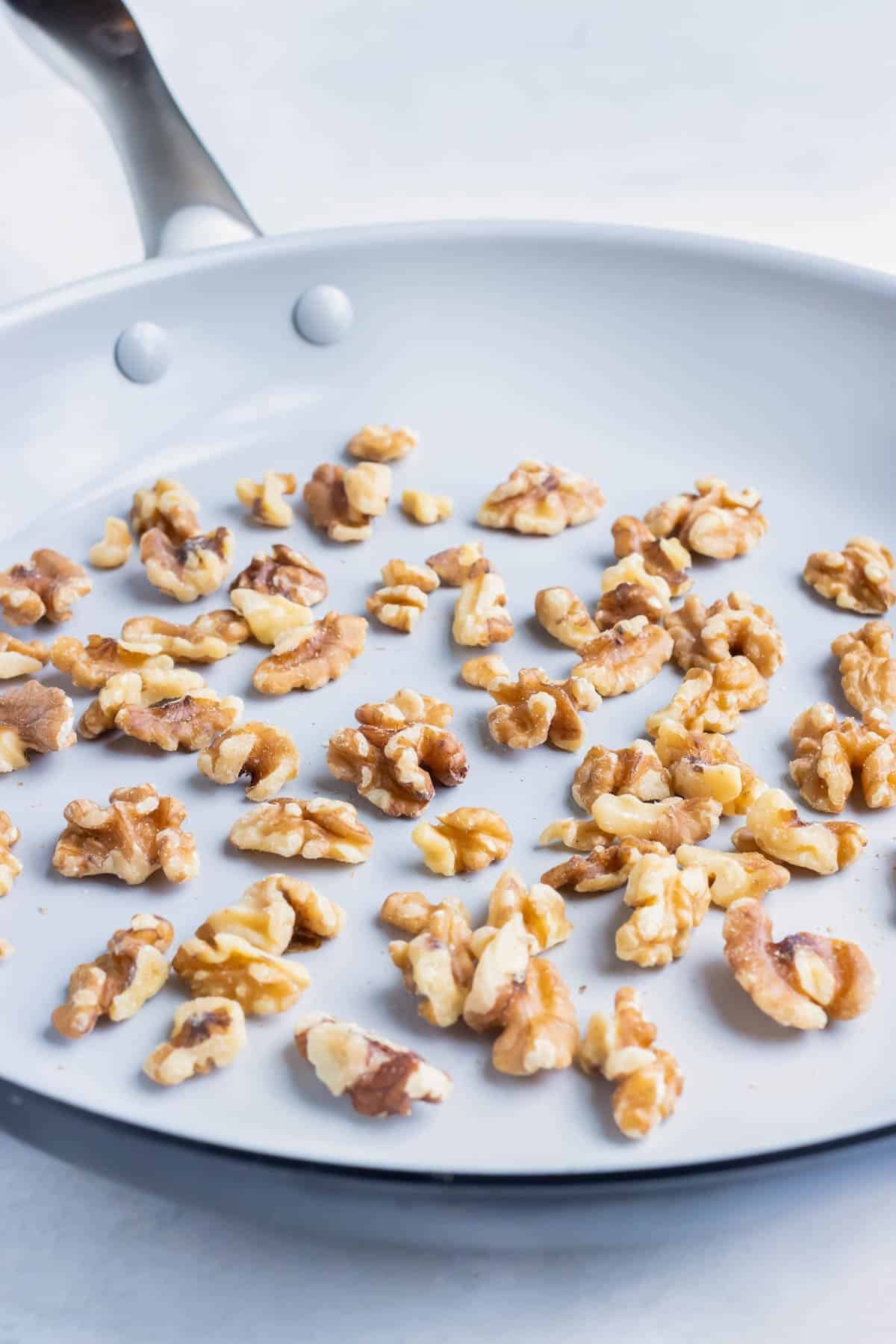 Walnuts are toasted in a skillet on the stove.