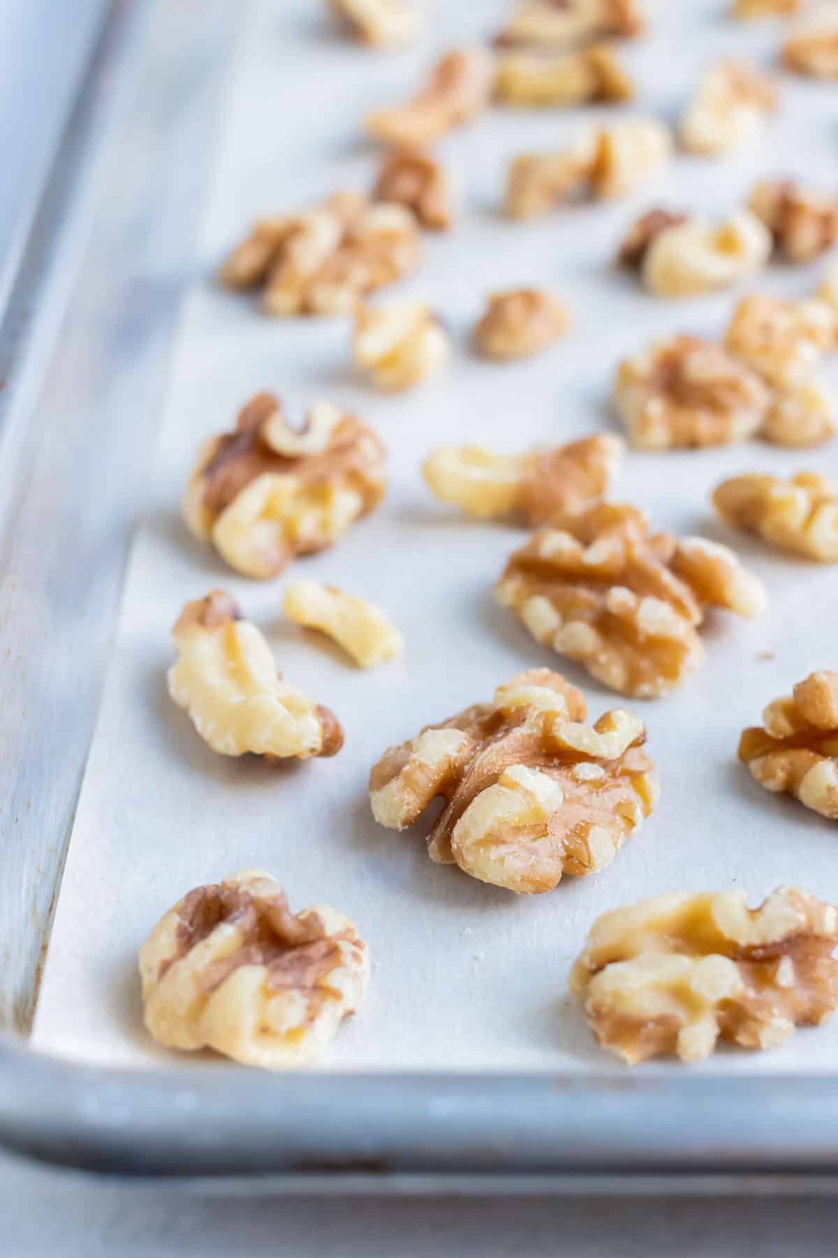 Walnuts are placed on a lined baking sheet and toasted in the oven.