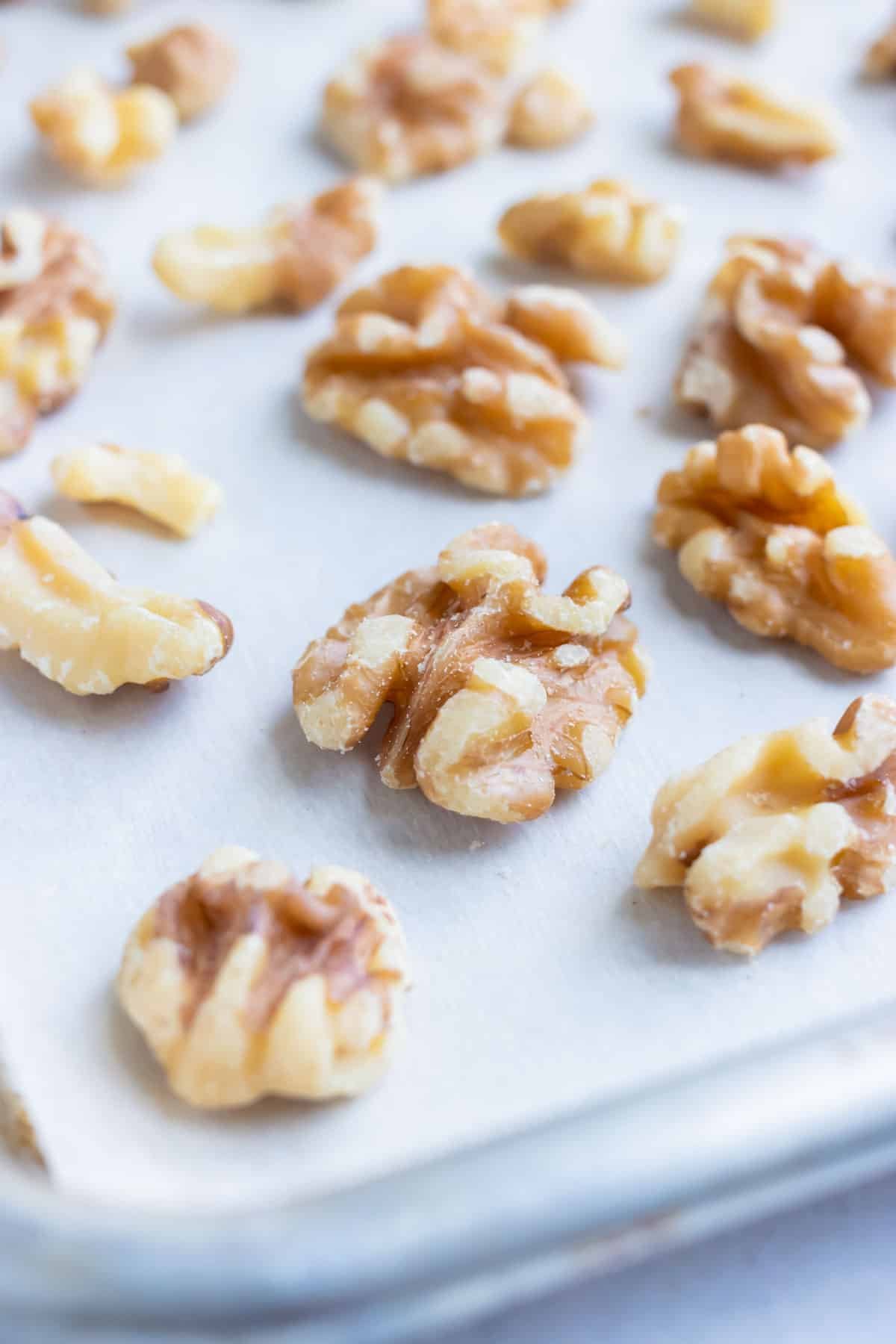 Raw walnuts are placed on a lined baking sheet and roasted in the oven.