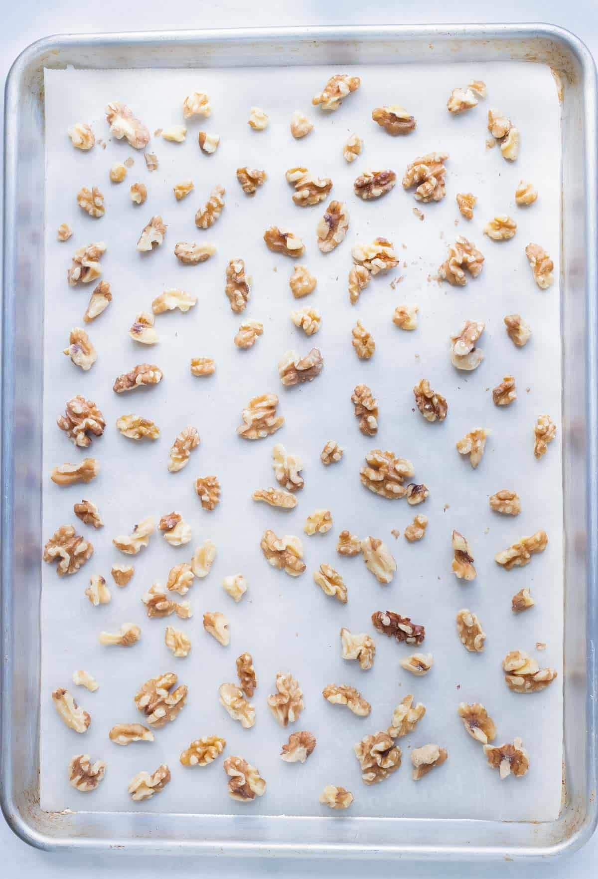 A parchment paper-lined baking sheet with walnuts scattered in a single layer.