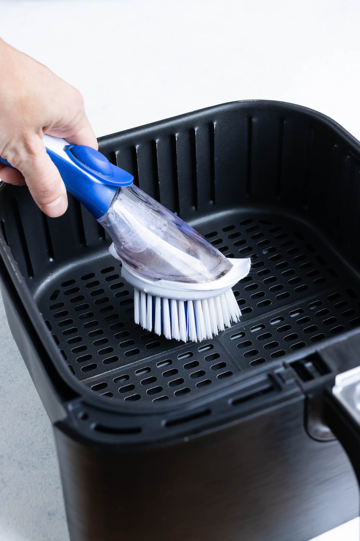 Scrubbing the air fryer basket with a soapy, soft bristle brush.