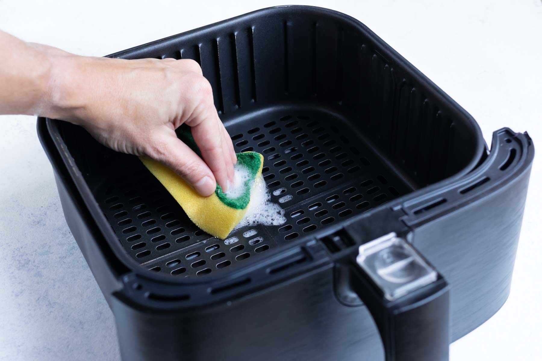 Wiping down the air fryer basket with a sponge brush.