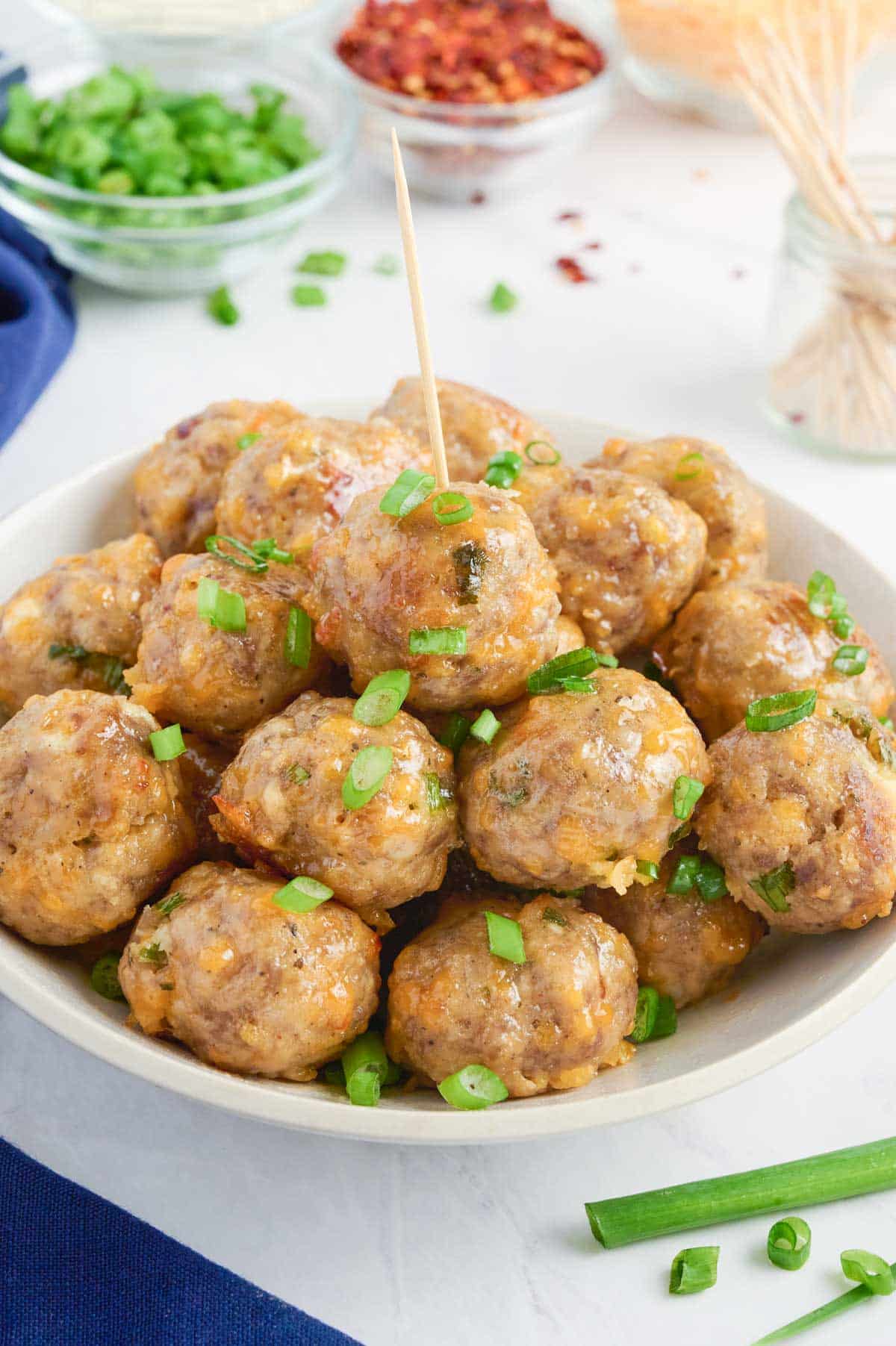 A toothpick is inserted into a sausage ball from a pile on a plate.