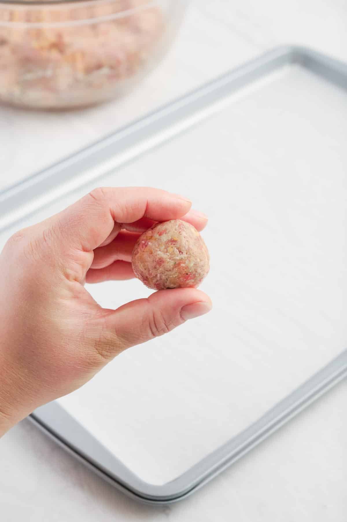 A hand rolls the sausage mixture into a ball.