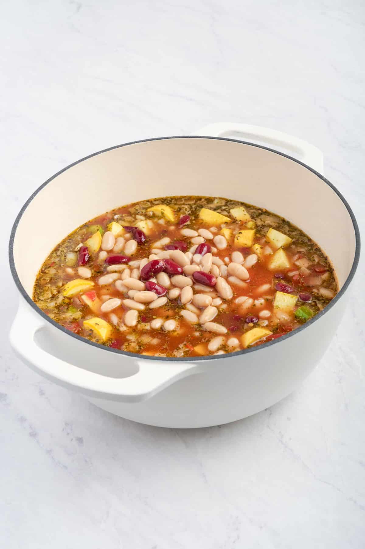 Red and white beans are added to a soup in a pot.