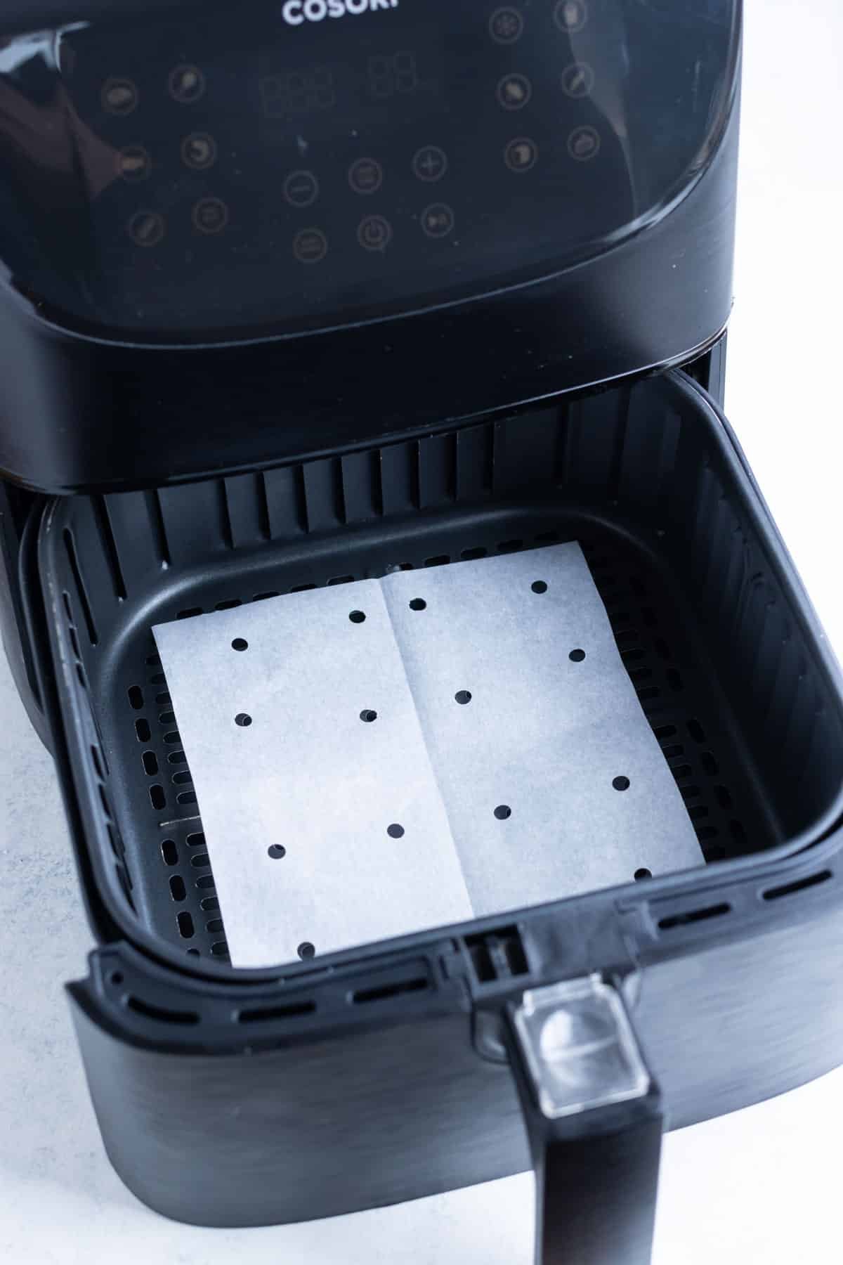 Parchment paper place in the bottom of an air fryer basket with hole punches.