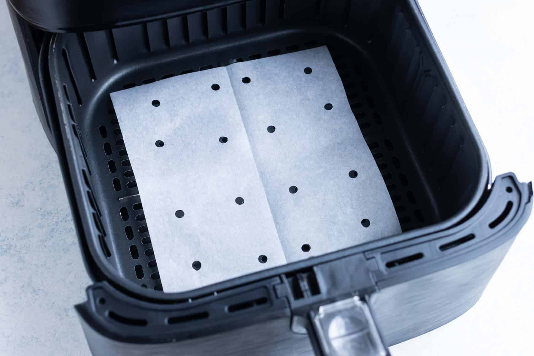 Parchment paper at the bottom of an air fryer basket with hole punches.