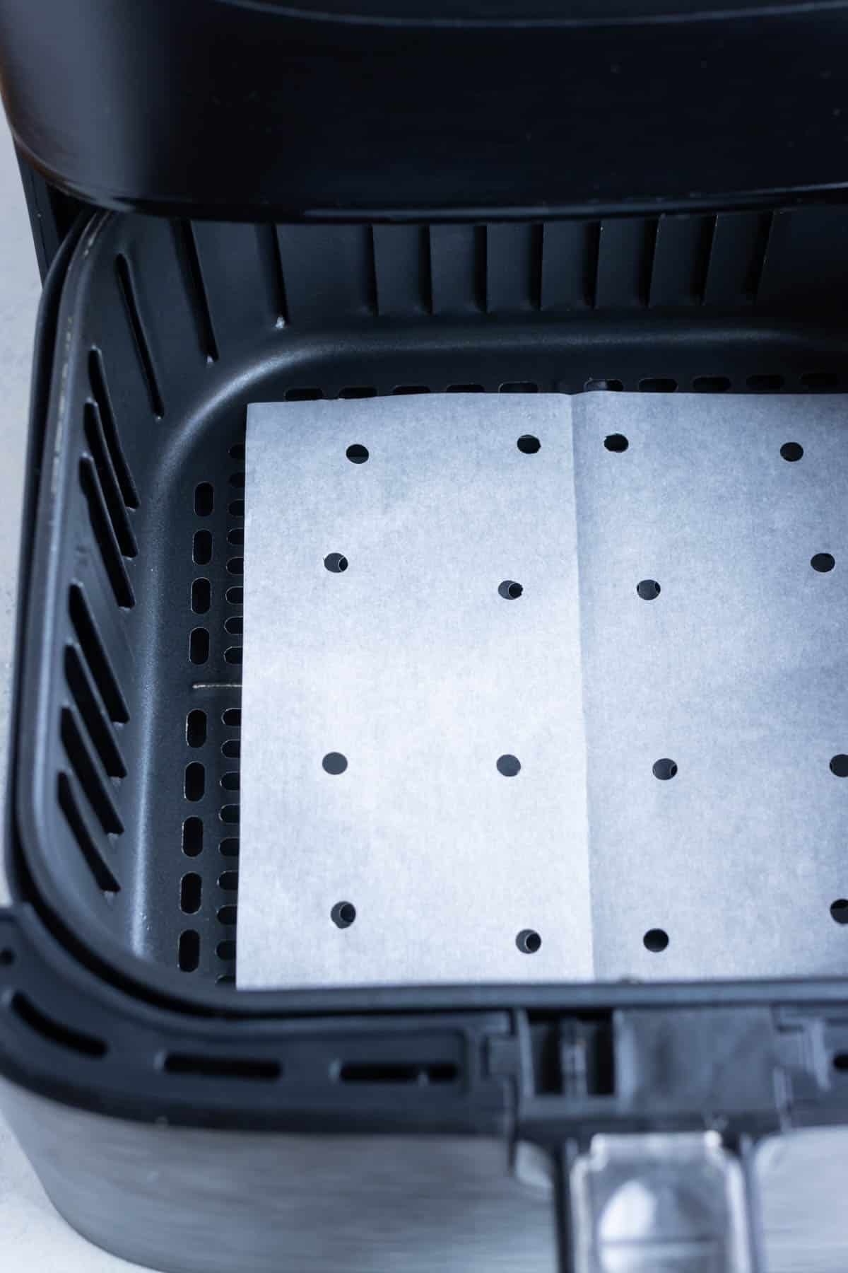 Parchment paper at the bottom of an air fryer basket with hole punches.