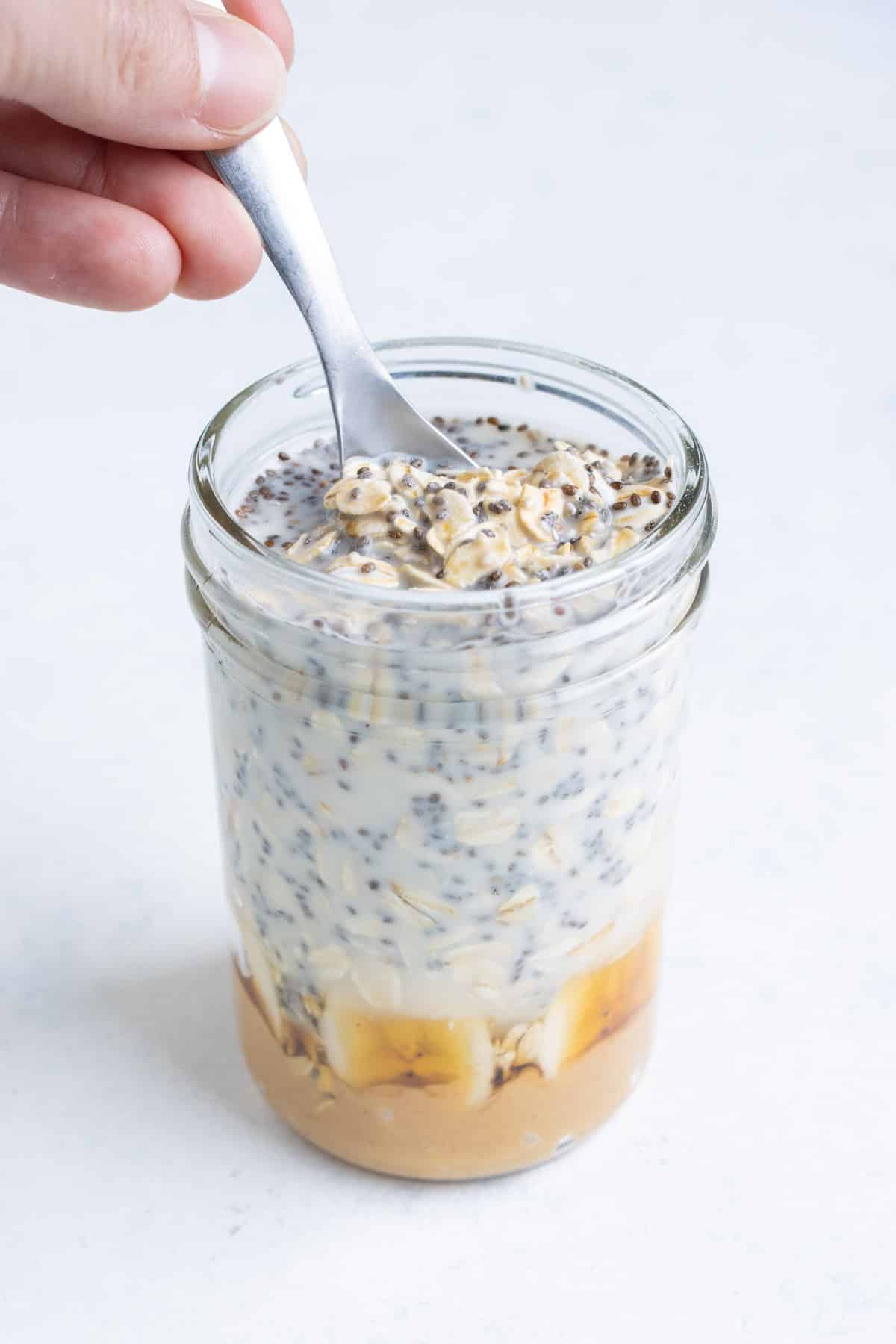 A spoon stirs the oatmeal mixture in a mason jar.
