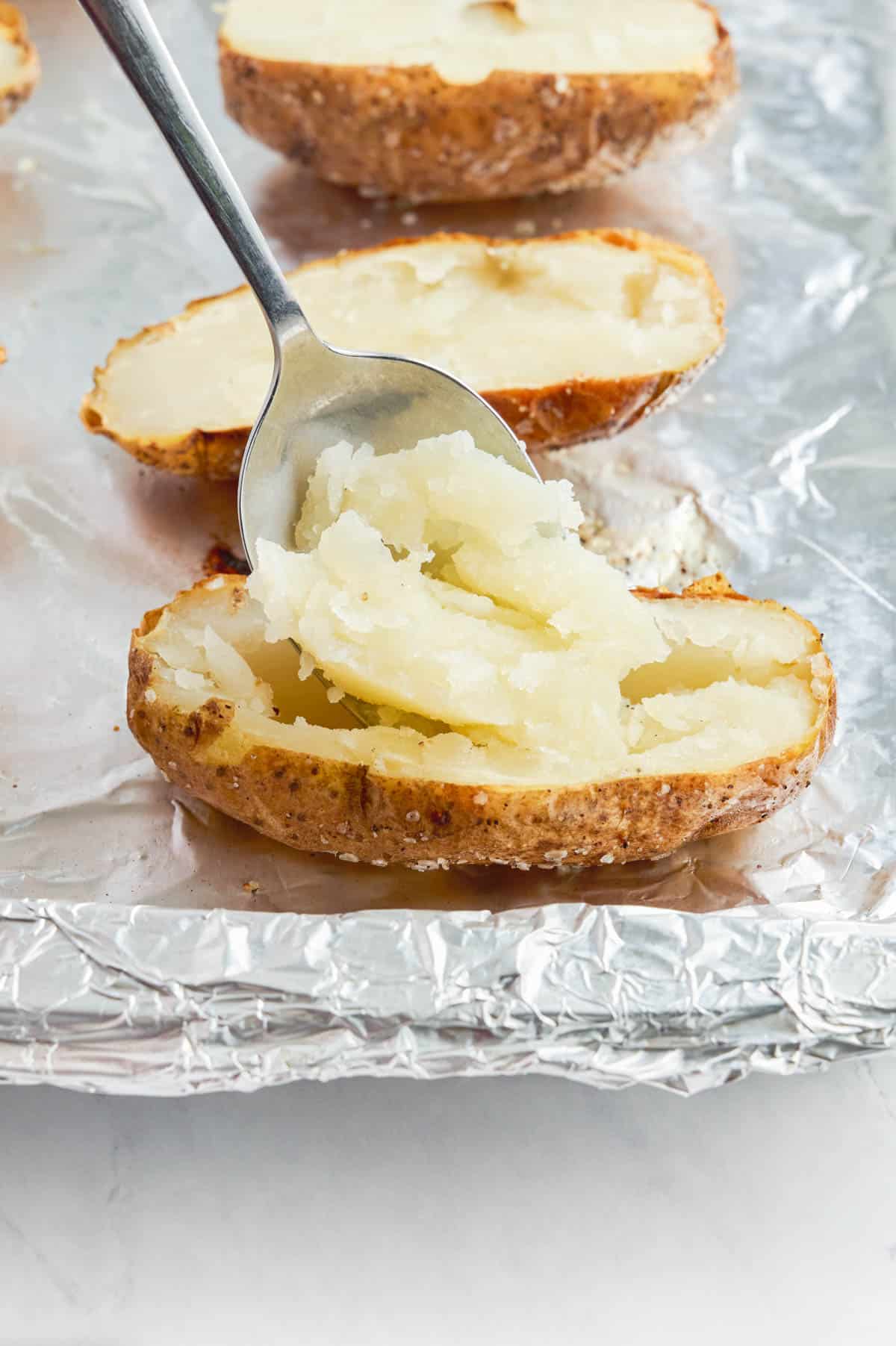 The insides of baked potatoes are scooped out with a spoon.