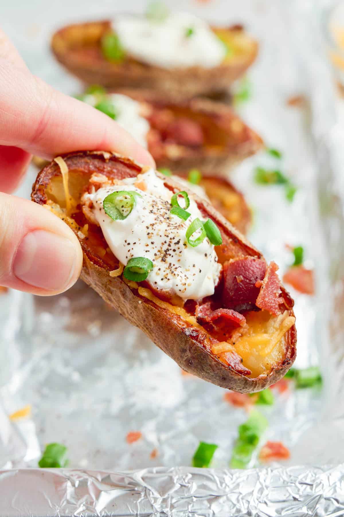 A hand holds a potato skin topped with sour cream and chives.