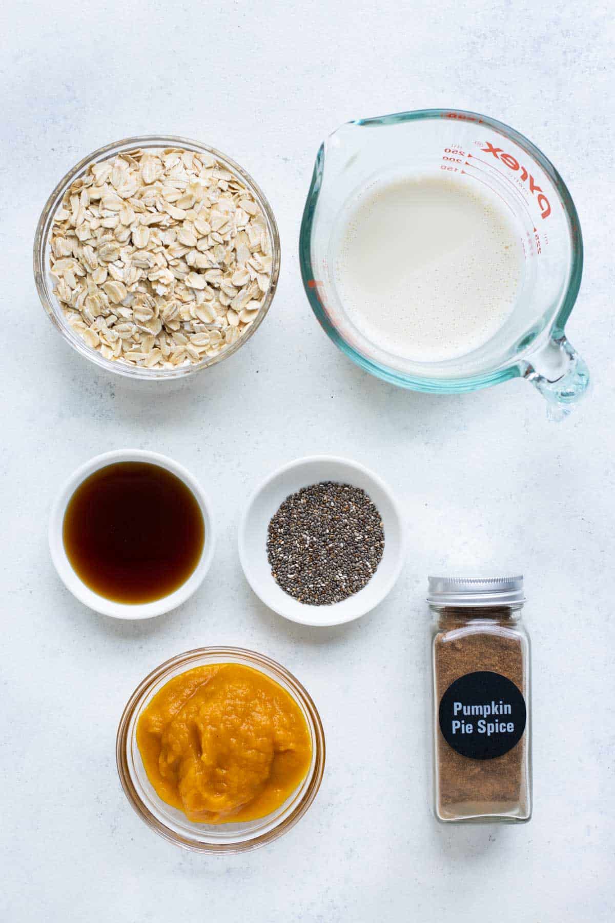 A top view of oats in a bowl with other ingredients like milk, chia seeds, maple syrup, and pumpkin to make overnight oats. 
