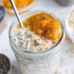 A close-up of a glass mason jar full of overnight oats, pumpkin pie spice puree, toasted pecans, and whipped cream.