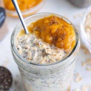 A close-up of a glass mason jar full of overnight oats, pumpkin pie spice puree, toasted pecans, and whipped cream.