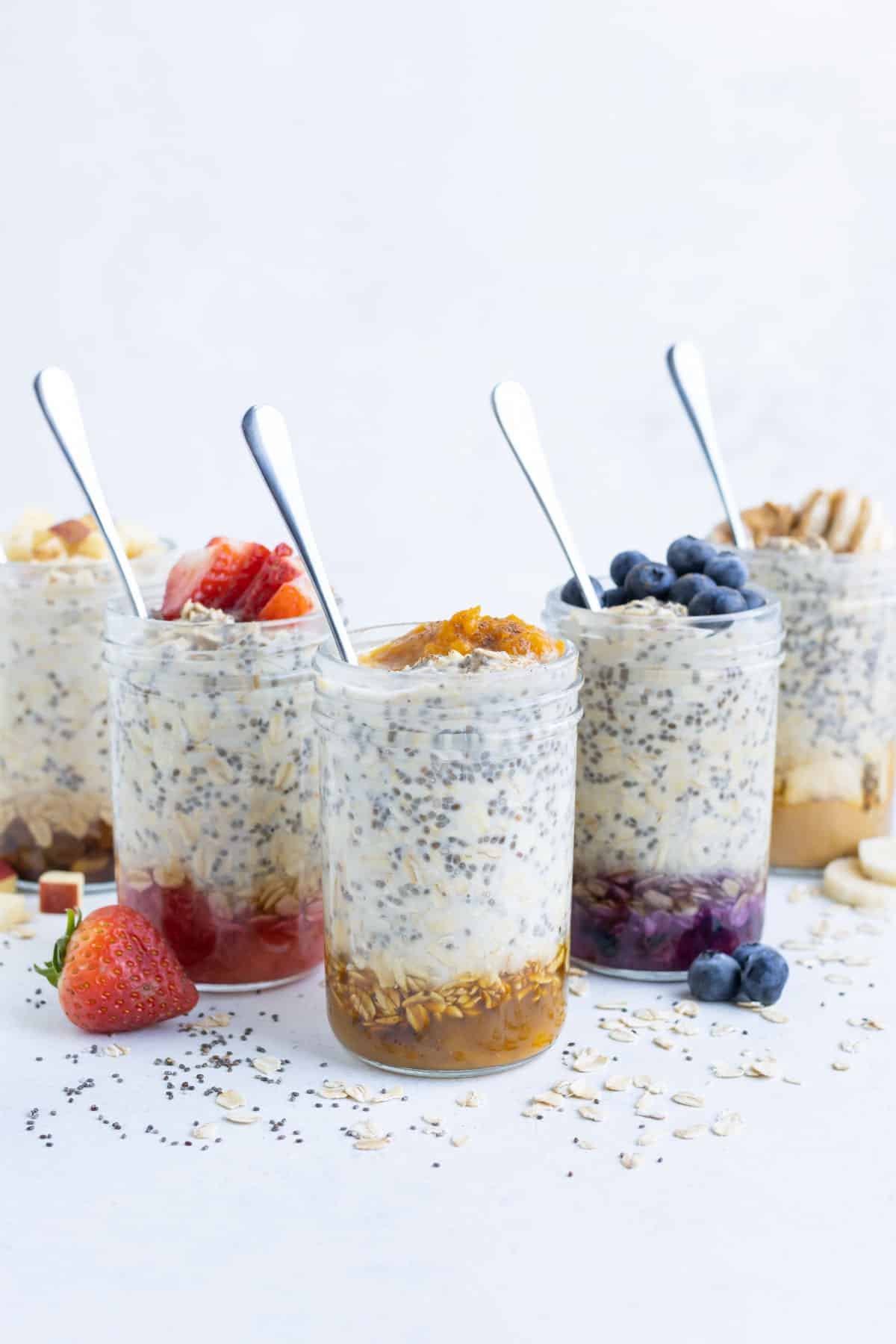 Pumpkin, blueberry, peanut butter, strawberry, and apple cinnamon overnight oats on a table.