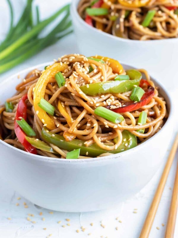 Cold sesame noodles with bell peppers in a white bowl with chopsticks and green onions next to it.