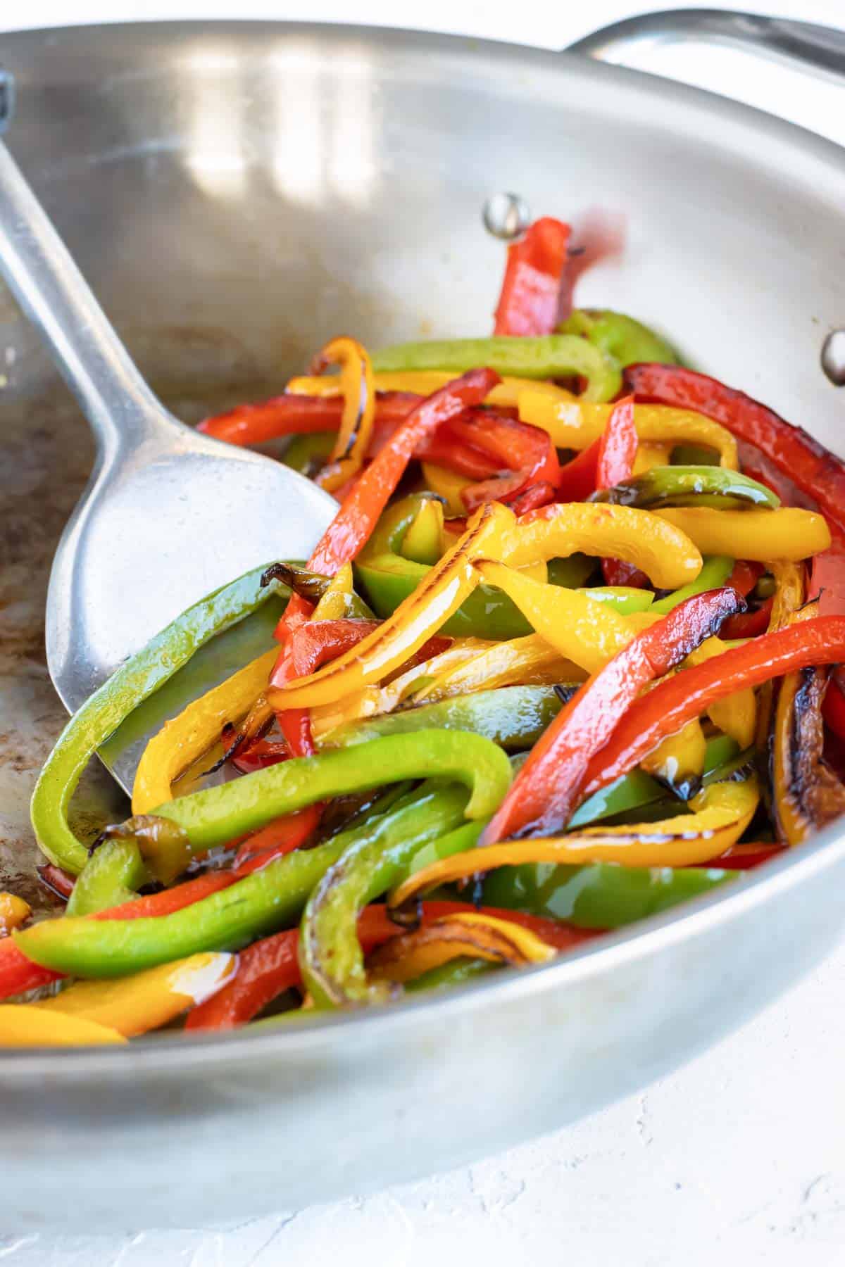 Sauteeing red, green, and yellow bell peppers in a stainless steel skillet.