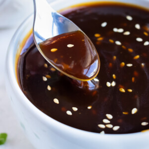 A spoon is lifting up some homemade sticky teriyaki sauce from a white bowl.