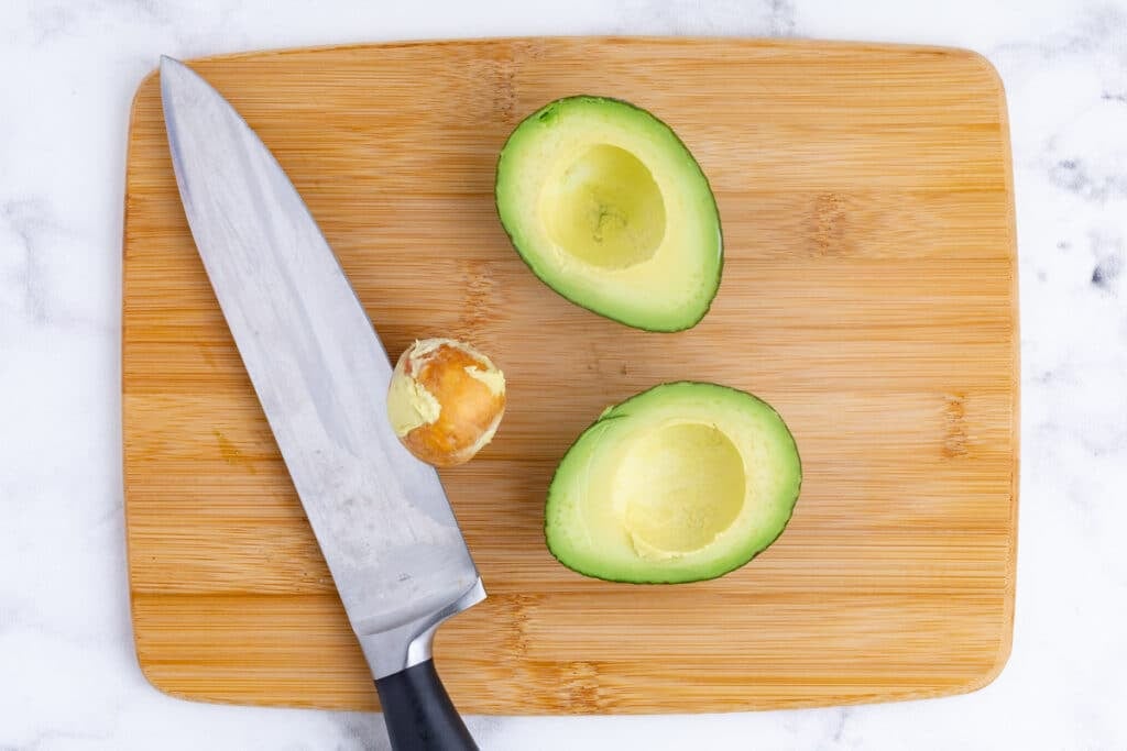An avocado halved and sliced into wedges on a cutting board.