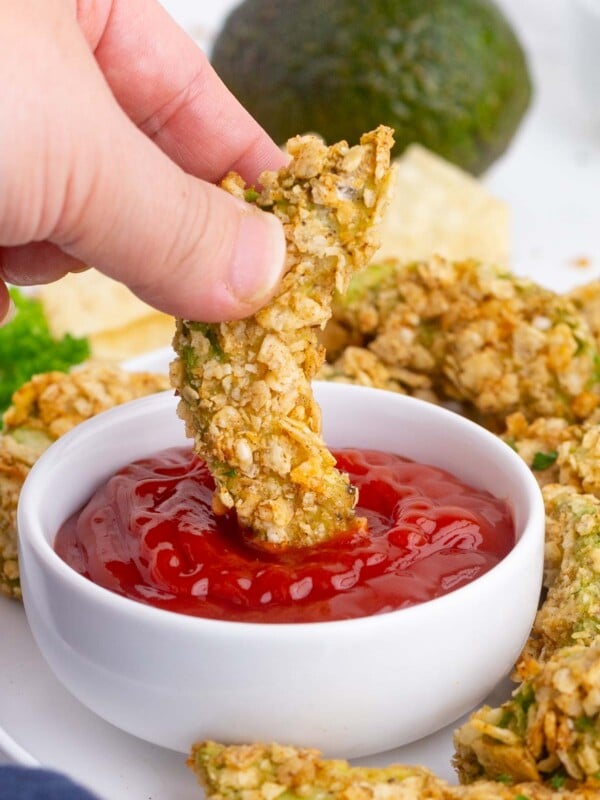 A hand dips an avocado fry into ketchup.