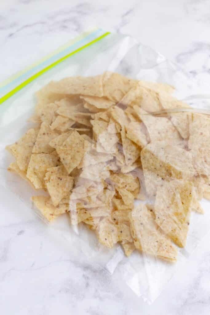 Tortilla chips in a bag being crushed for the avocado fry coating.