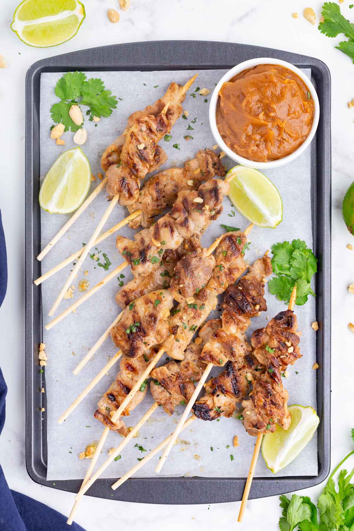 A tray with a pile of chicken satay skewers and peanut dipping sauce.