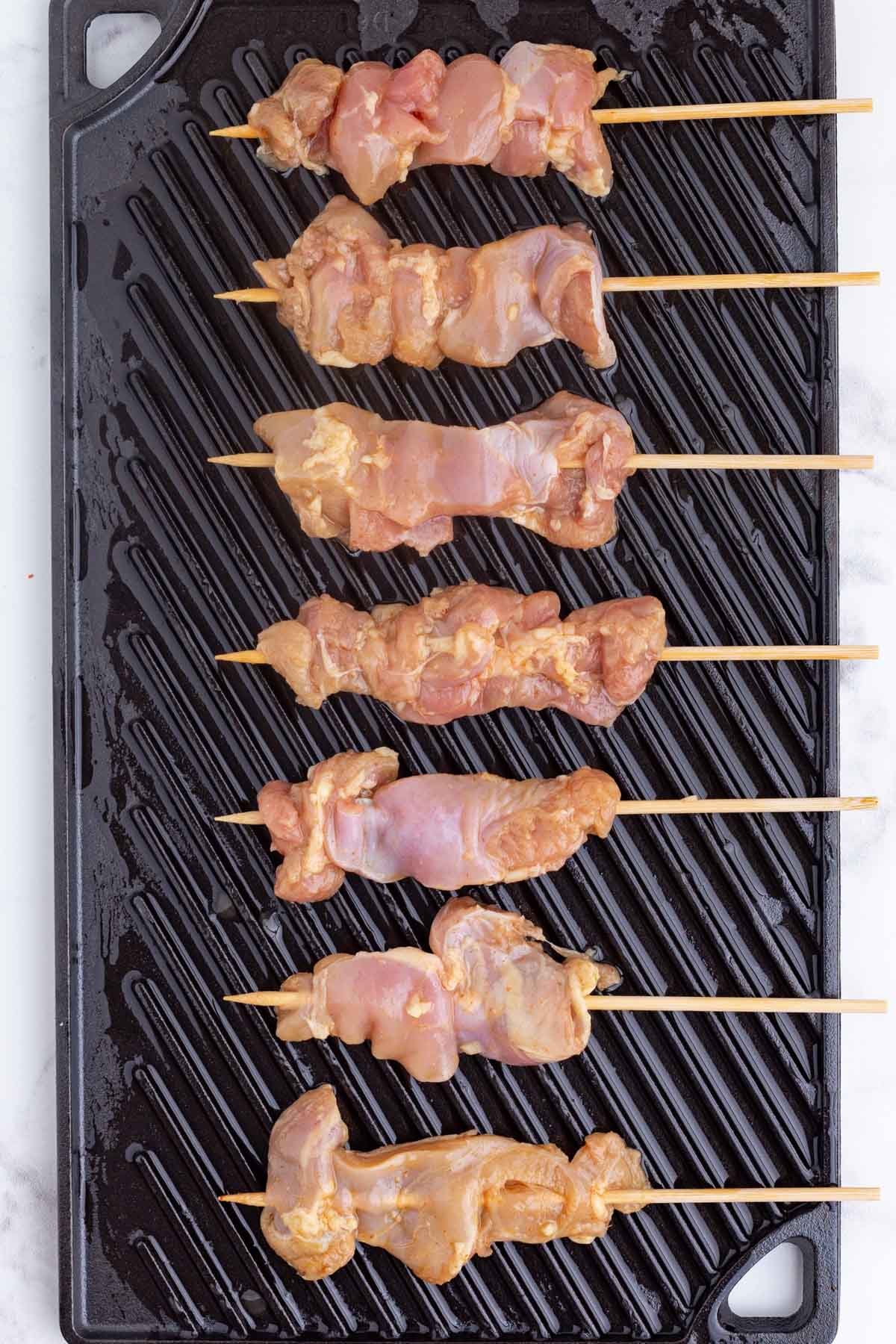 Chicken skewers are placed on a grill plate.