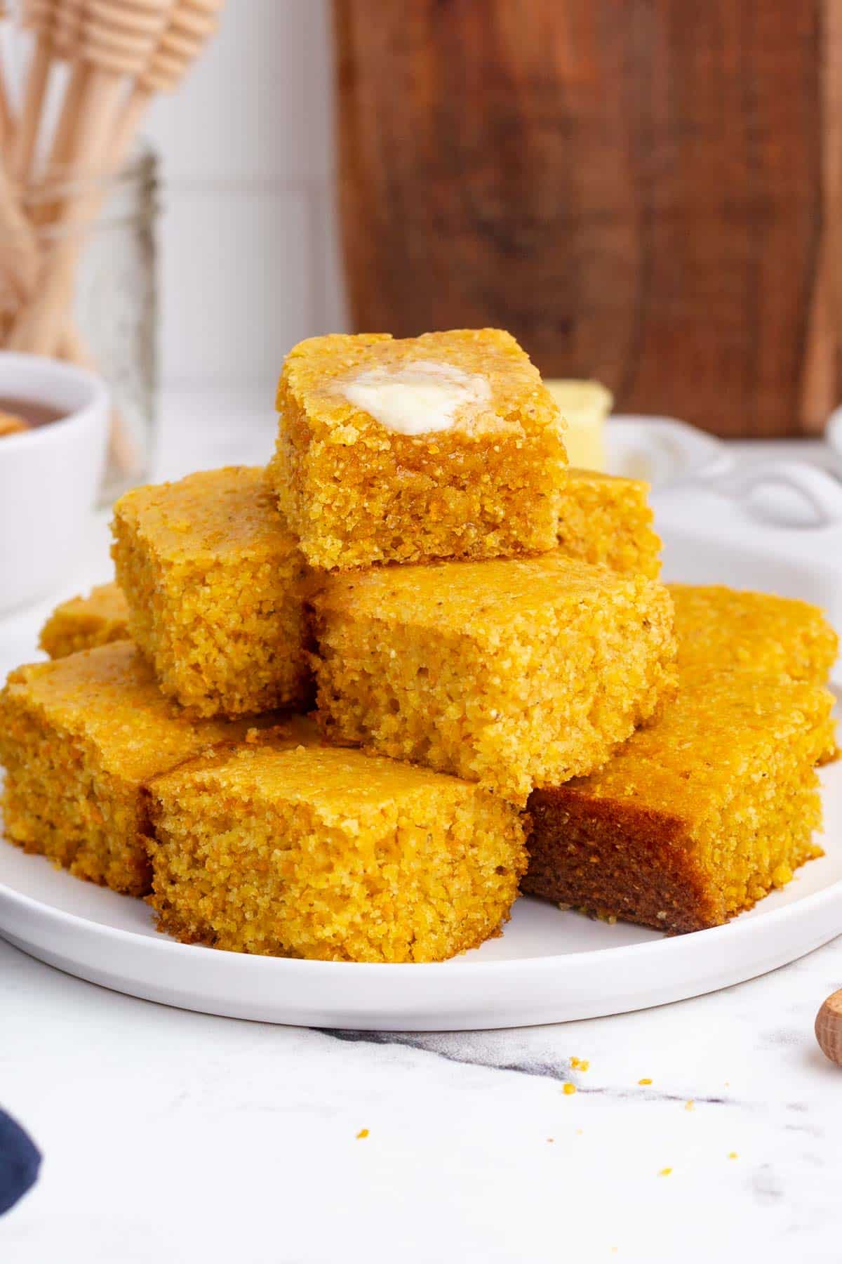 A stack of cornbread slices are on a white plate.