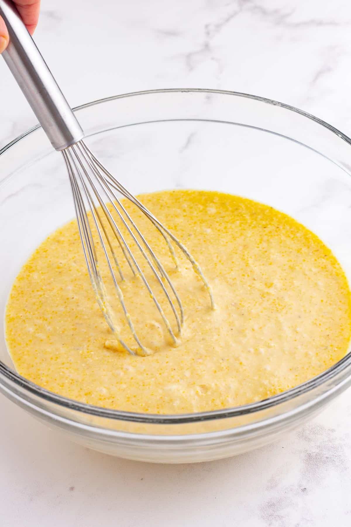 A whisk stirs cornbread batter.