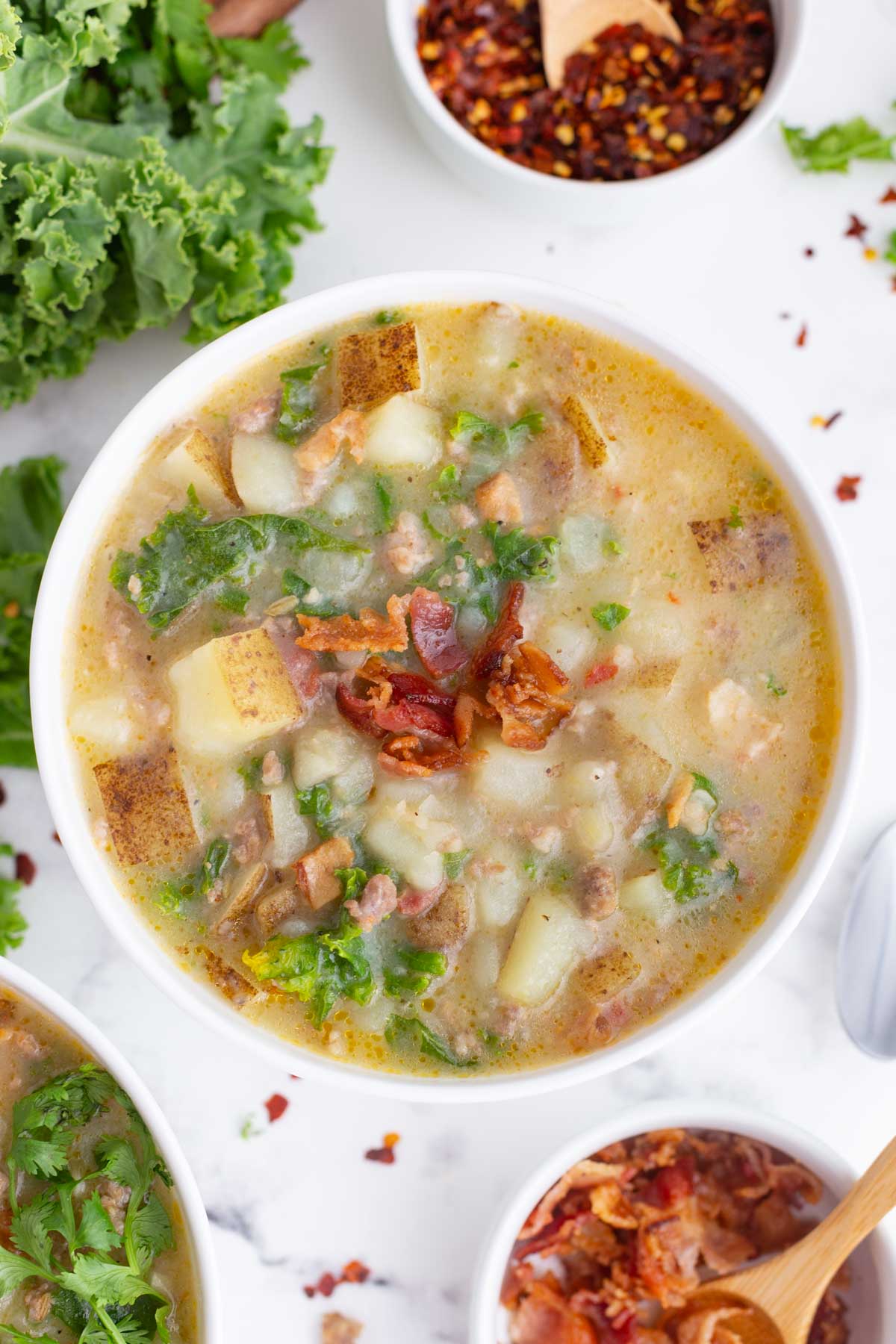 A copycat recipe for Olive Garden zuppa toscana soup in a white bowl with a hand holding it.