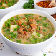 A copycat recipe for Olive Garden zuppa toscana soup in a white bowl with a hand holding it.