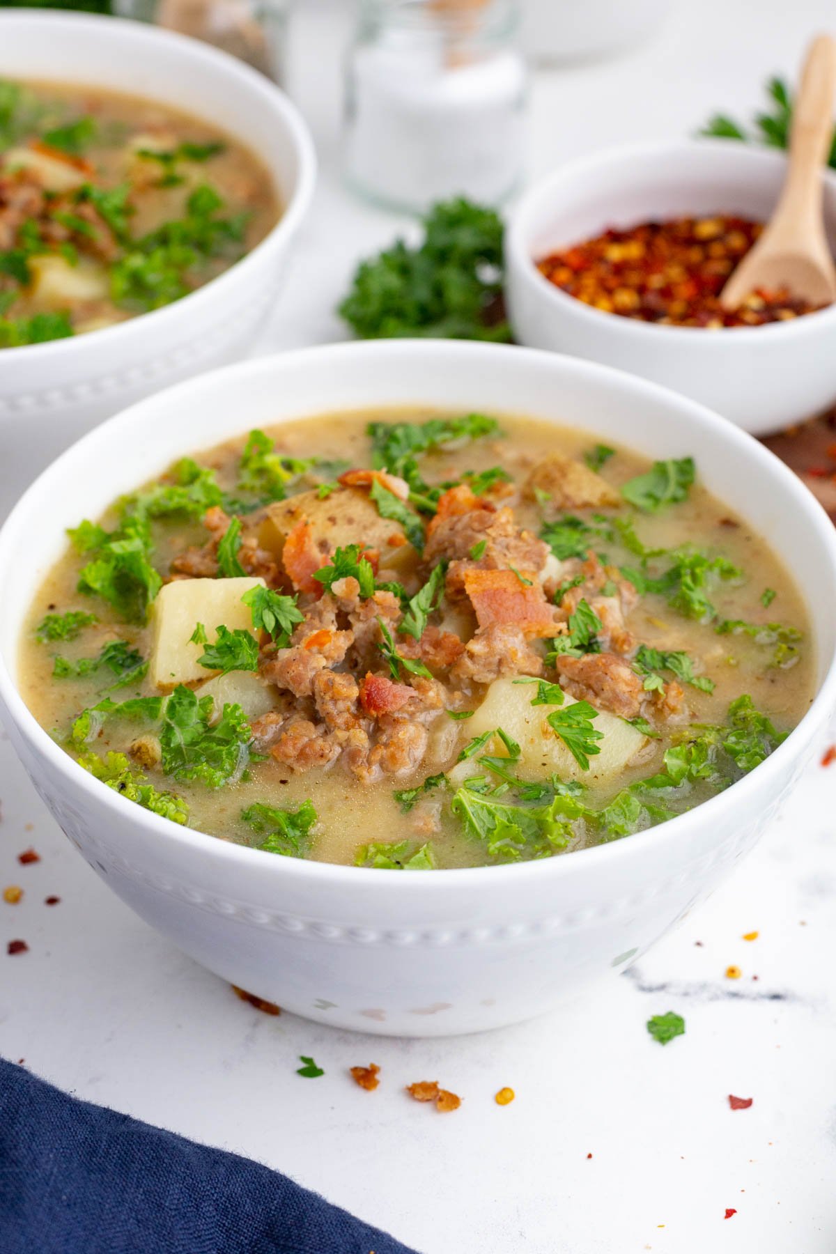 A copycat recipe for Olive Garden zuppa toscana soup in a white bowl with a hand holding it.