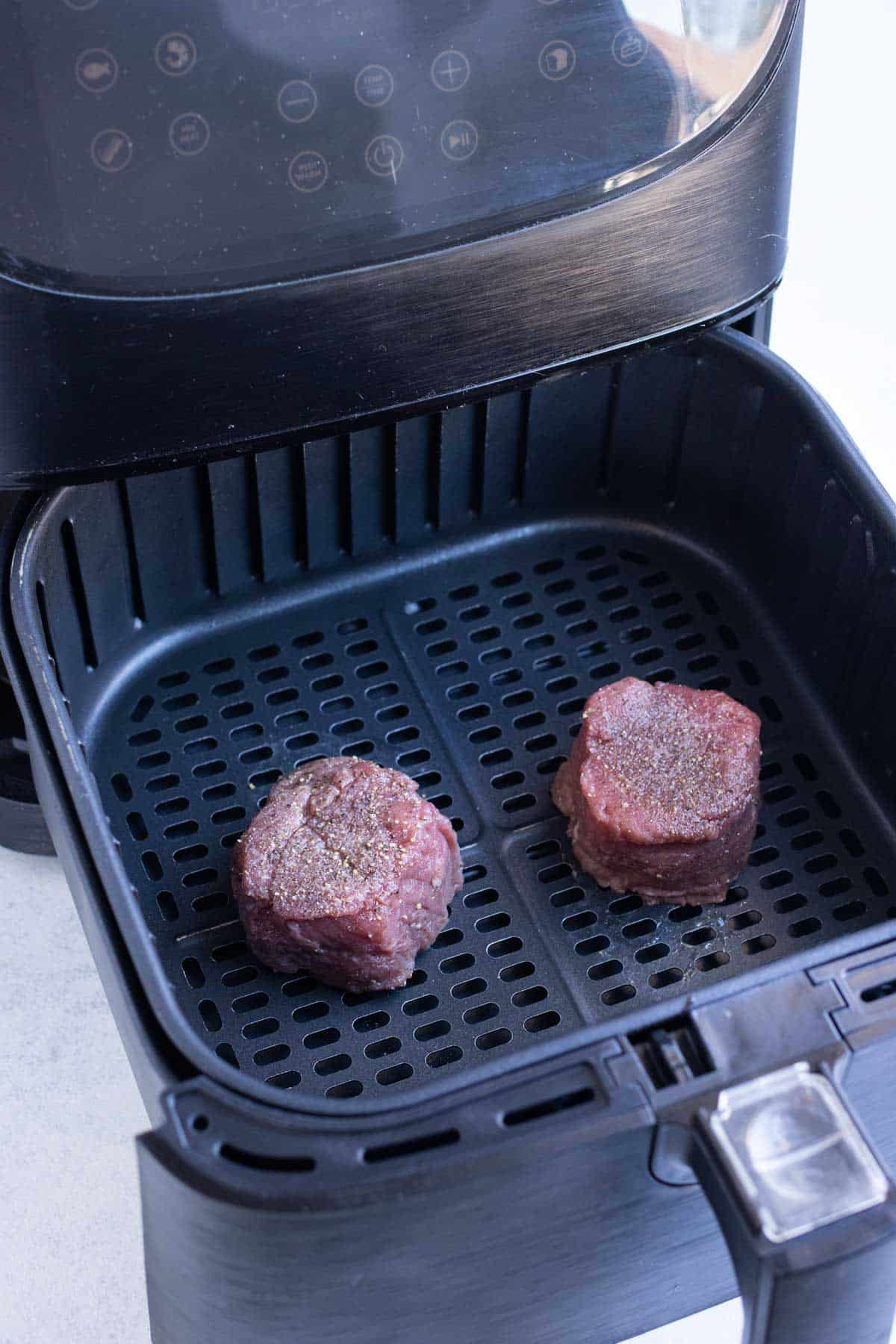 Two pieces of steak are placed in the air fryer.