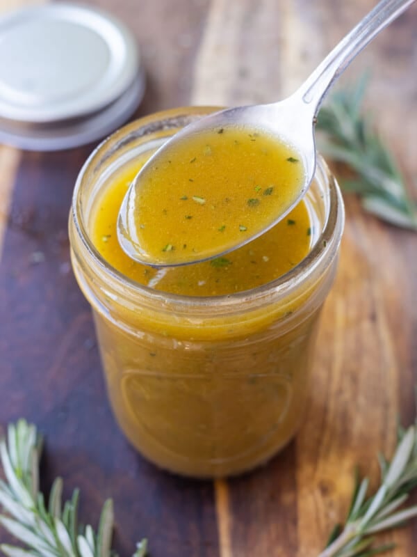 An apple cider vinaigrette has been shaken up in a jar and a spoon scoops it out.