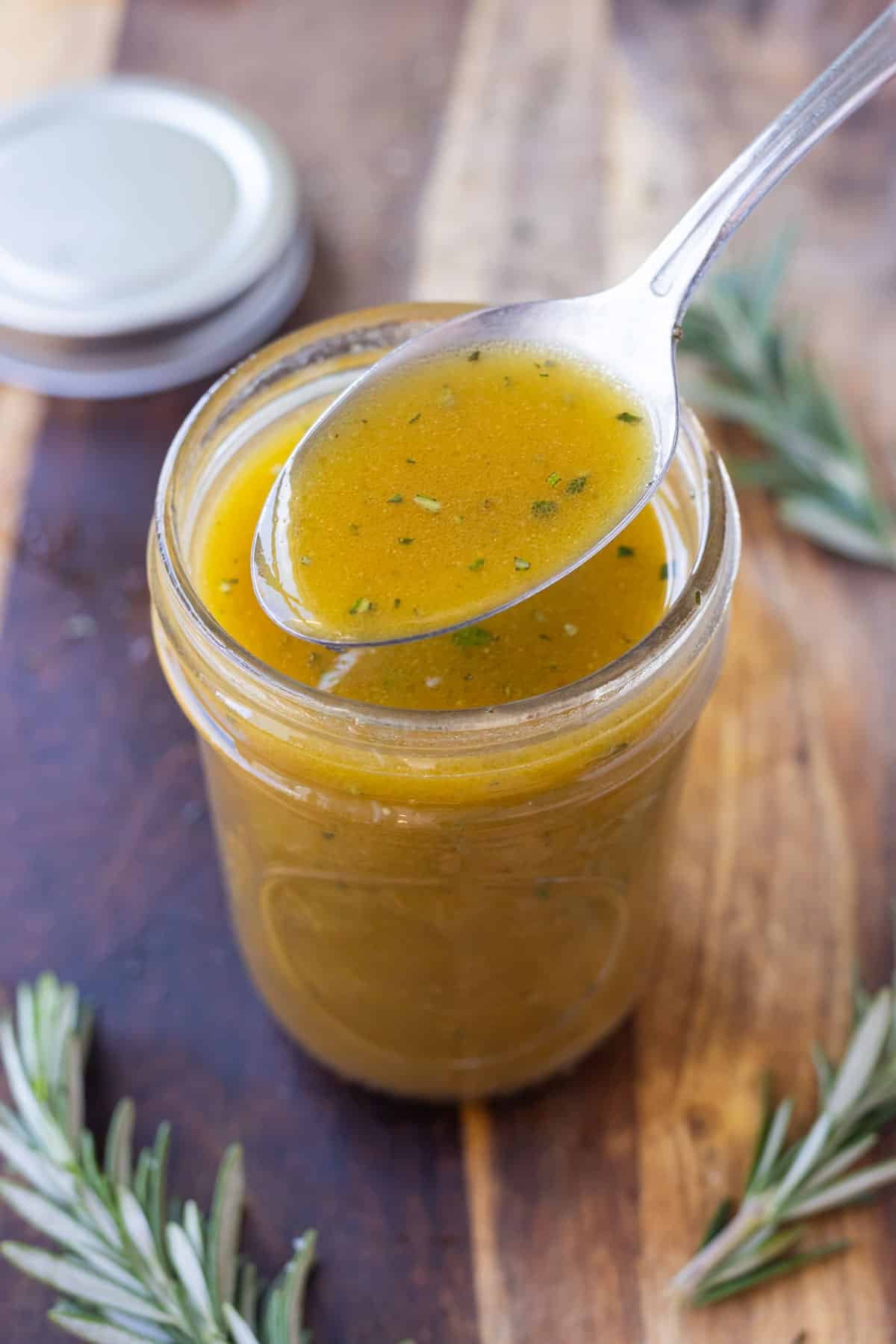 An apple cider vinaigrette has been shaken up in a jar and a spoon scoops it out.