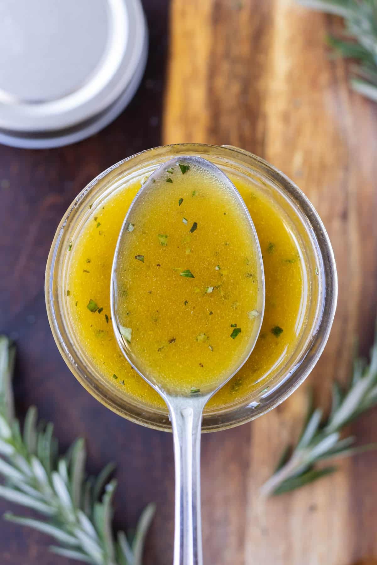 A spoon is holding some homemade apple cider vinaigrette salad dressing on top of a mason jar.