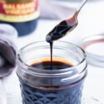 A healthy balsamic glaze recipe being scooped up from a glass jar with a spoon.